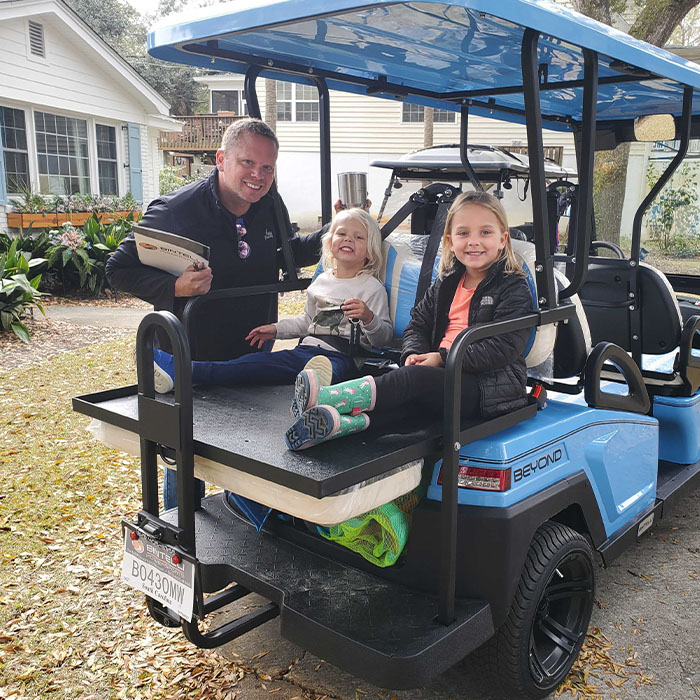 A Family enjoying their brand new Bintelli A 6 seater street legal golf cart in ocean blue parked on their driveway. They also have a Family enjoying Bintelli A 6 seater street legal golf cart in Titanium