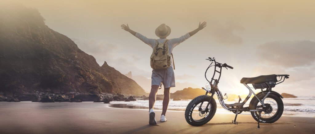 A man standing next to the bintelli electric bike on a beach