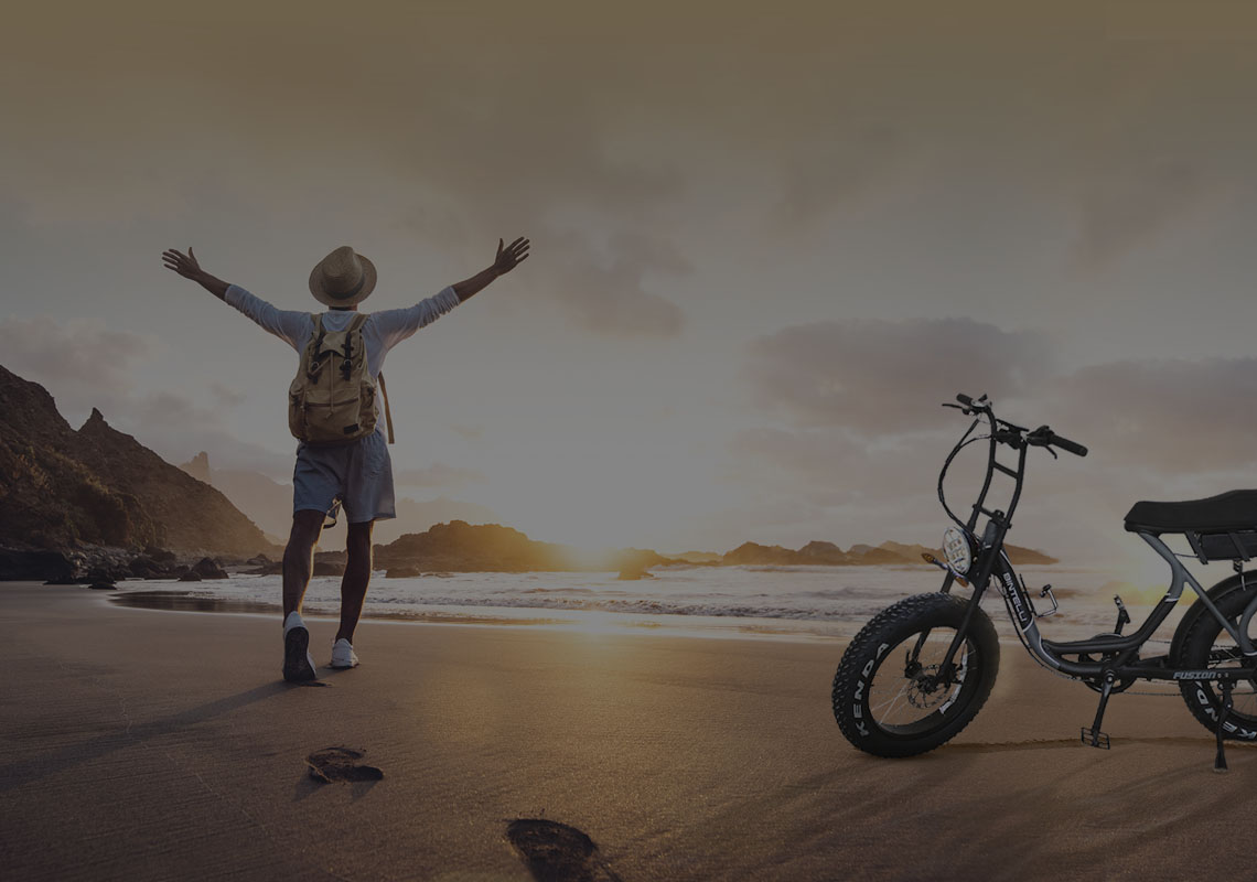 Man rode his Bitnelli electric bike to the ocean. He watches the sunset happily while his electric bike is parked next to him.